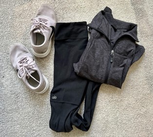 Image shows a pair of black Alo Yoga leggings, a neutral-colored sweat-wicking jacket and a white running sneakers