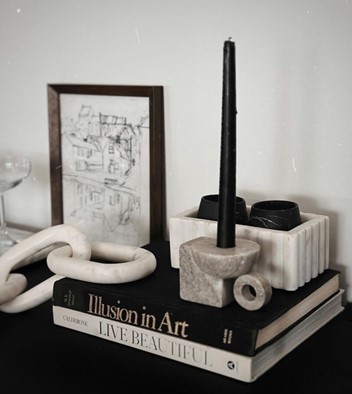 Two books one with a black cover and one with a white cover used as decor next to a candle and a picture frame