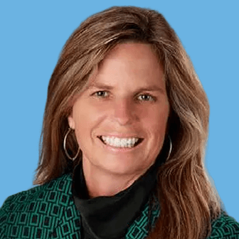 Smiling woman with long light brown hair wearing a green patterned blazer and black top, against a bright blue background.