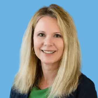 Smiling woman with shoulder-length blonde hair, wearing a green top and dark blazer, against a blue background.