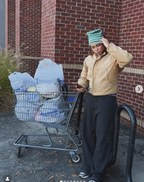 Women wearing a bege jacket and green hat pushing a cart full of bags 