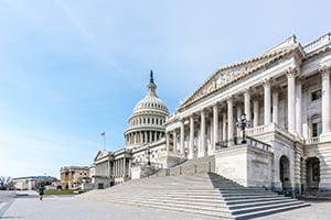 United States Capitol with grand staircase and neoclassical wing under a clear blue sky.