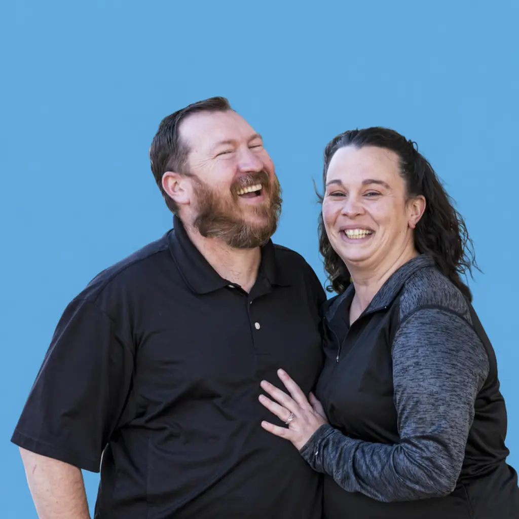 Two cheerful adults stand together against a blue background with milestone badges highlighting Goodwill impact.